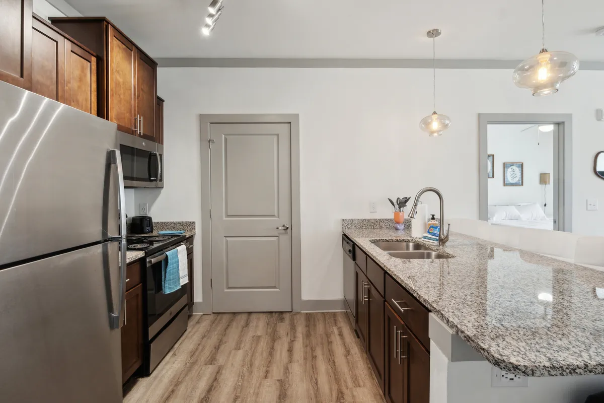 A modern kitchen featuring a spacious island with granite countertops, stainless steel appliances, and sleek cabinetry. The scene is set for socializing, with bar stools at the island and hints of morning rituals like coffee cups ready for use.