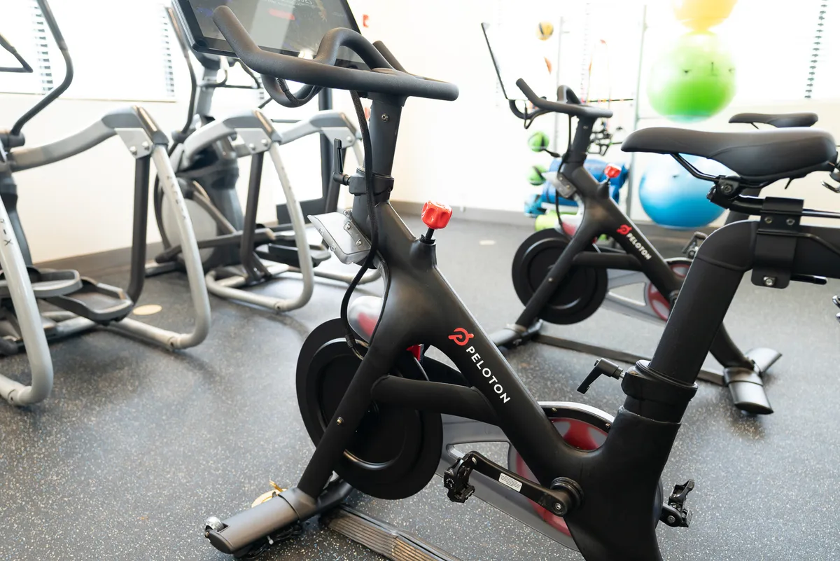 A bright fitness center with Peloton bikes, elliptical machines, and colorful exercise balls set against large windows. The atmosphere is energetic and welcoming, motivating residents to engage in active, healthy routines.
