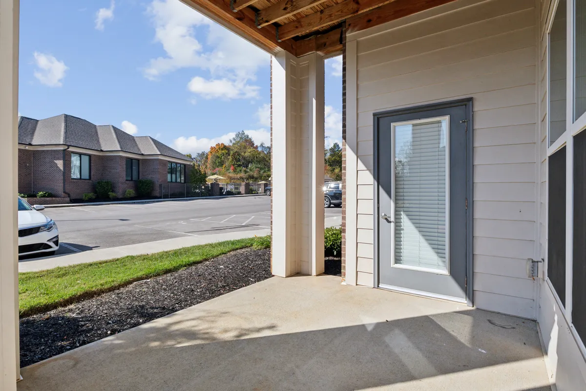 This image shows the front door of Overlook 5106, framed by a neatly landscaped area and an adjacent parking lot. The entryway is bright and welcoming, suggesting easy arrival and departure for residents. The visible parking area connects directly to the convenience the section emphasizes.