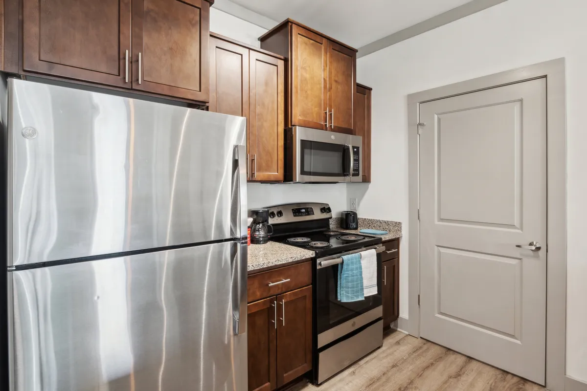A view of the kitchen showcasing a stainless steel refrigerator, granite countertops, wood cabinetry, and modern appliances. The space is arranged for both cooking and entertaining, with subtle details like a coffee mug on the counter and a bowl of fresh fruit, conveying a welcoming, lived-in feel.